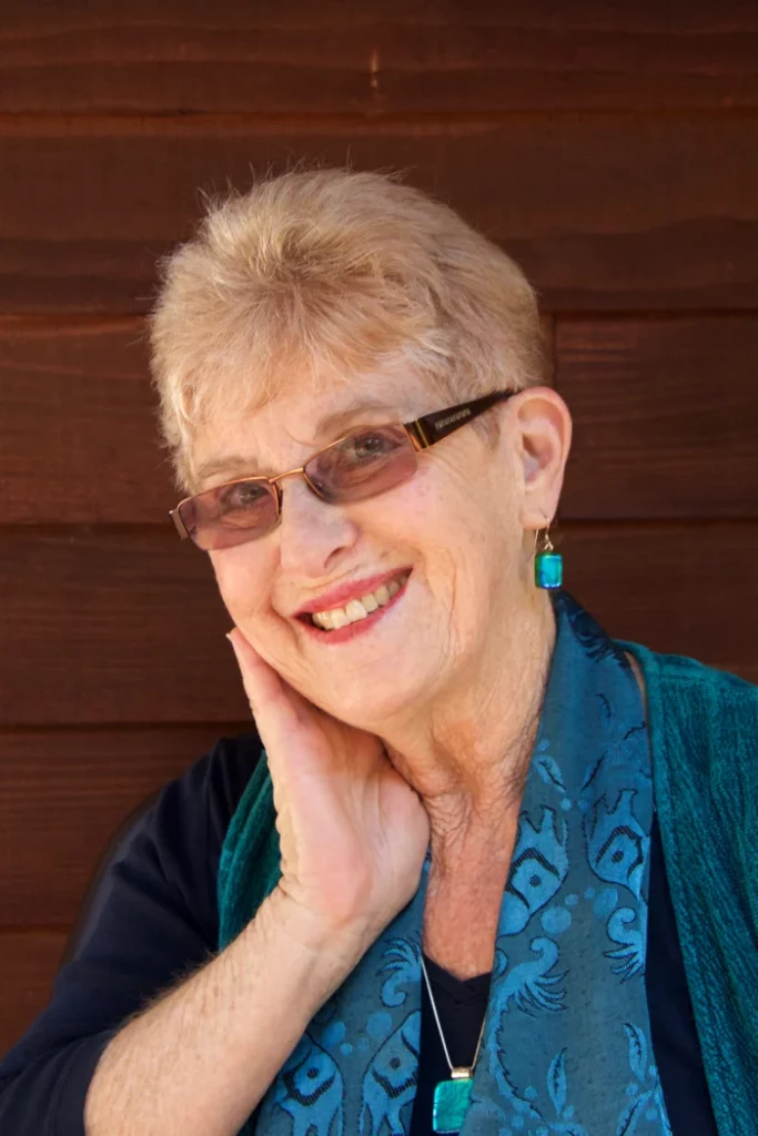 Author Paula Wagner smiling in front of a wooden wall, wearing a teal scarf and matching jewelry.